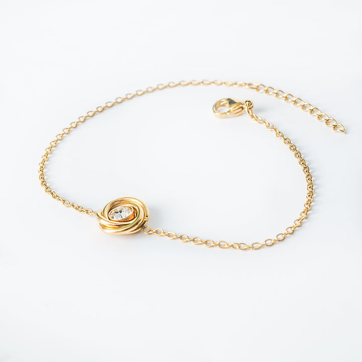 Gold chain bracelet with a knot-style pendant featuring a clear round crystal
