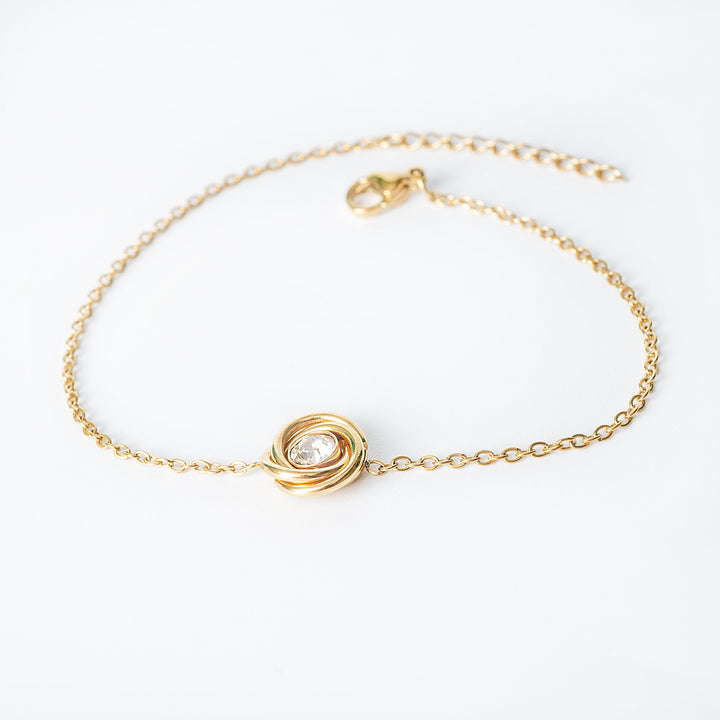 Gold chain bracelet with a central knot-style pendant featuring a clear round crystal