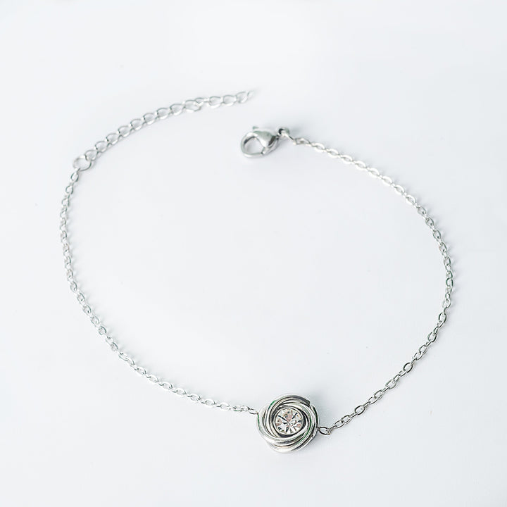 Silver chain bracelet with a knot-style pendant holding a clear round crystal