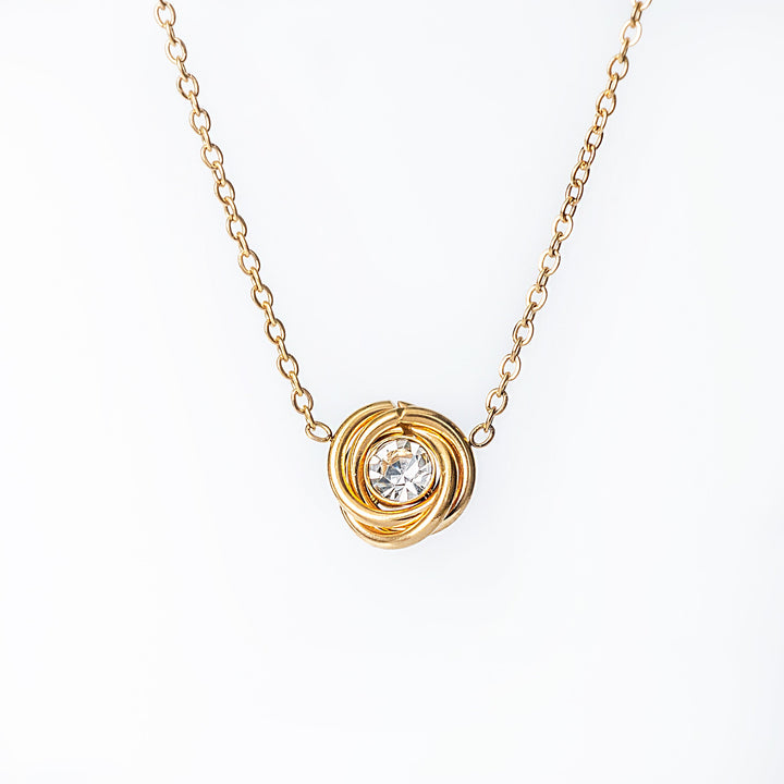 Gold necklace with a knot-style pendant featuring a clear round crystal in the center