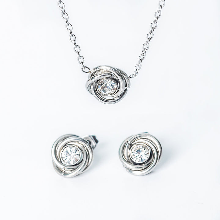 Silver jewelry set with necklace and earrings featuring circular designs and clear stones on a white background.
