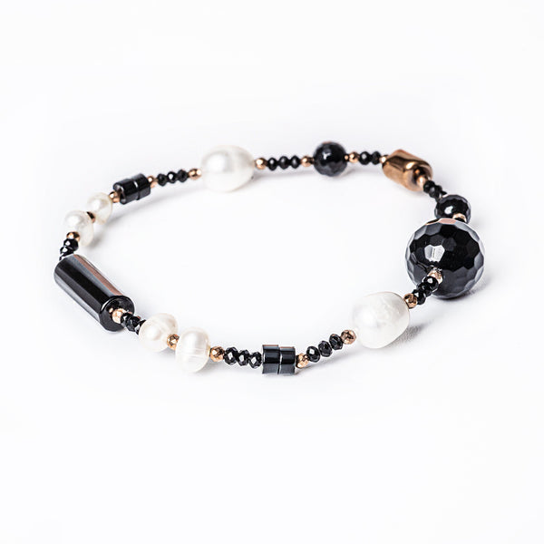 A bracelet with a mix of pearls, beads in black, white, and rose gold colors, and a large central stone.