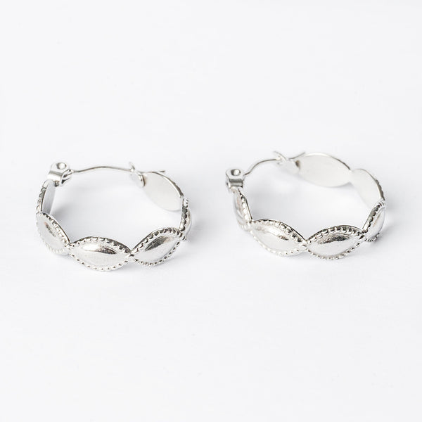 A pair of silver Nakita hoop earrings with intricate detailing, displayed against a white background.