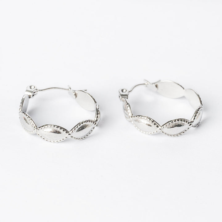 A pair of silver Nakita hoop earrings with intricate detailing, displayed against a white background.