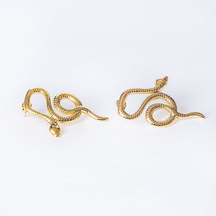 A pair of gold-plated stainless steel Nixi earrings designed to resemble a snake, displayed against a white background.