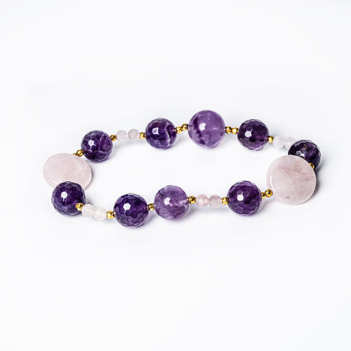 A bracelet with a gold plated stainless steel band and an orchid-colored gemstone bead, accompanied by smaller clear and pink beads.