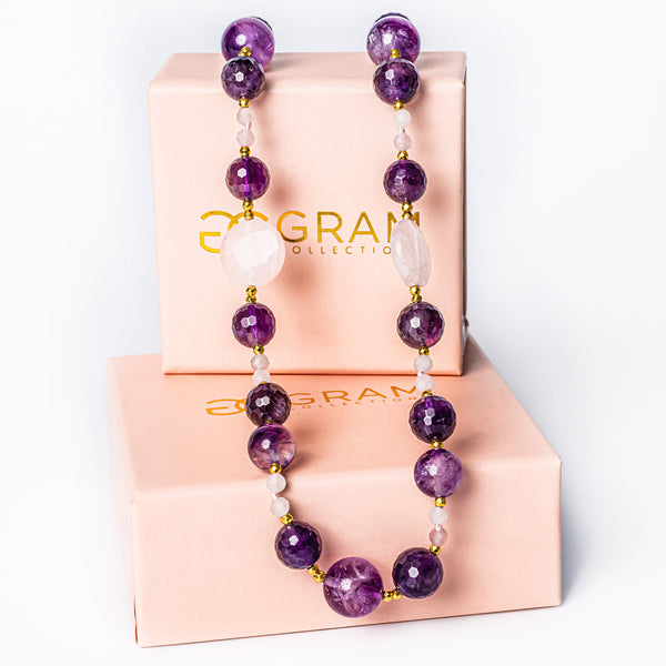 An Orchid Necklace standing in the center of the image placed on its uniquely designed pink box. 