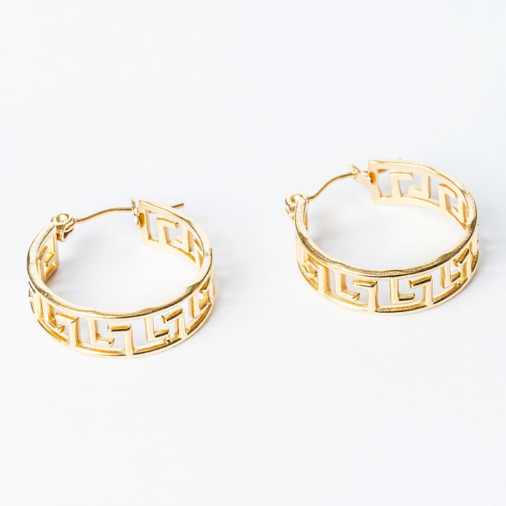 A close up view of Paulette gold earrings standing in the center of the image against a white background. 