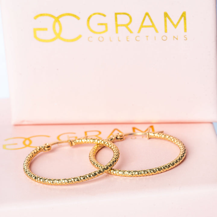 A close up view of claudia earrings, standing in the center of the image, placed on its uniquely designed pink box.  