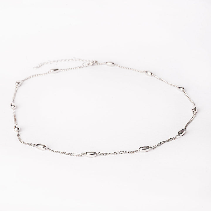 Silver pisa necklace standing in the center of the image against a white background. 