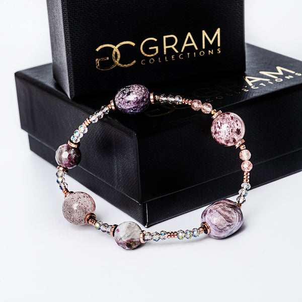 A plum bracelet placed on the edge of its uniquely designed box. 