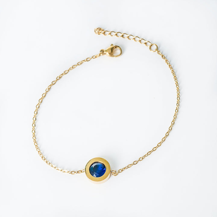Gold Rosaria bracelet with a deep blue round gemstone in a bezel setting
