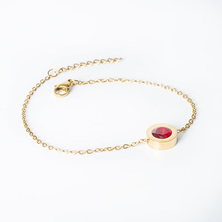 Gold Rosaria bracelet with a red gemstone centerpiece on a fine chain