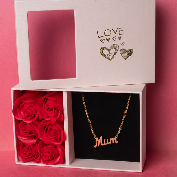 Rosina mum necklace with a gold-plated pendant, engraved with the word 'Mum', presented in a white box with 'LOVE' and hearts design, accompanied by a doily and red roses.