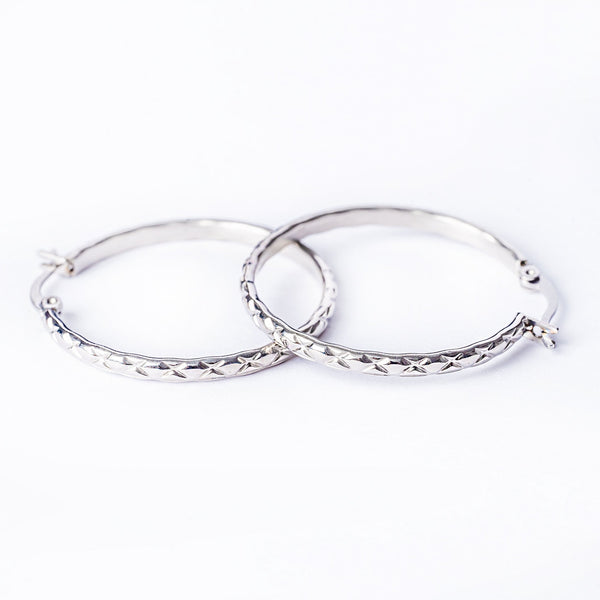 A pair of silver-colored stainless steel hoop earrings with a textured surface, displayed against a white background.