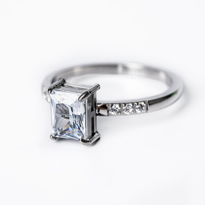 A silver-colored stainless steel ring with a gold plated band and a large central cubic zirconia gemstone surrounded by smaller clear crystals.