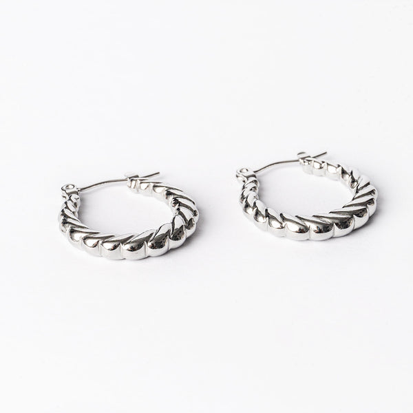 A pair of silver-colored stainless steel hoop earrings with a textured surface, displayed against a white background.