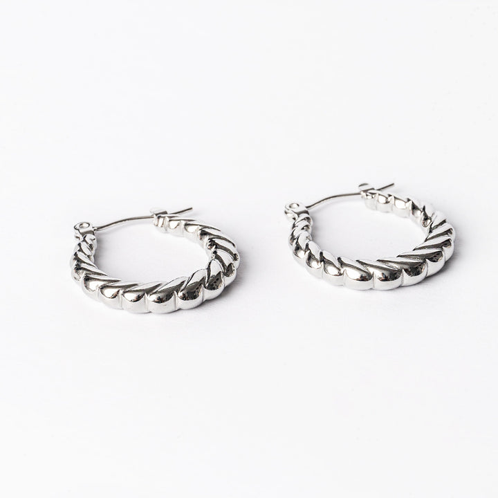 A pair of silver-colored stainless steel hoop earrings with a textured surface, displayed against a white background.