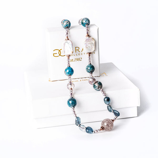 A teal necklace standing in the center of the image against a white backgroundplaced on its box. 