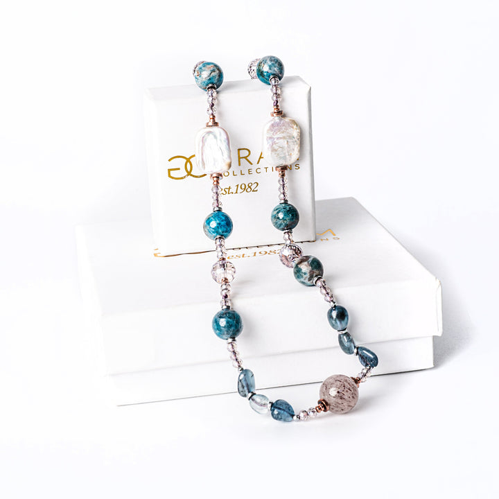 A teal necklace standing in the center of the image against a white backgroundplaced on its box. 