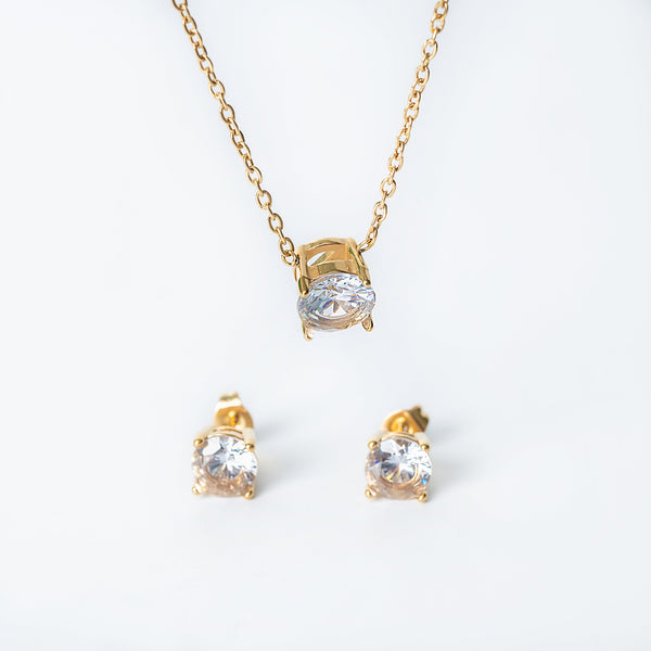 Gold Tessa jewelry set featuring a necklace with a single clear gemstone pendant and matching stud earrings.