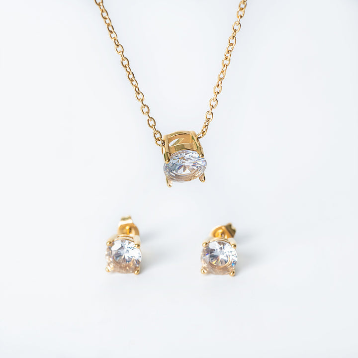 Gold Tessa jewelry set featuring a necklace with a single clear gemstone pendant and matching stud earrings.