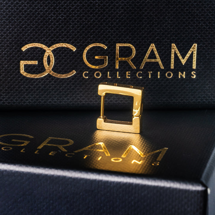 A single yellow gold-plated stainless steel Conor earring with a square design placed on a black box.