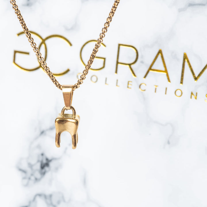 The The Dentist Necklace standing on the left side of the image in front of its uniquely designed white colour box. 