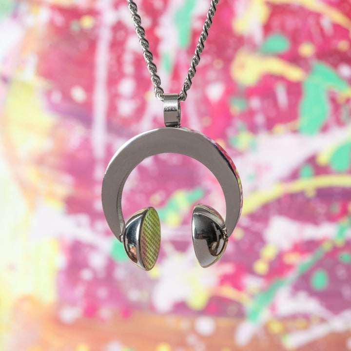 The dj necklace standing in the center of the image against blured colorful bakcground that consist of green, yellow and red colour mixed together. 