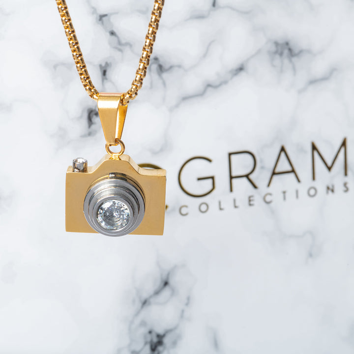 The Photographer Necklace standing in the left side of the picture, in front of its uniquely designed black box.