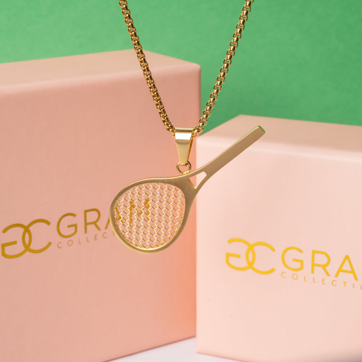 the tennis necklace hanging int the center of the image in front of its uniquely designed pin boxes, surrounded by green background. 