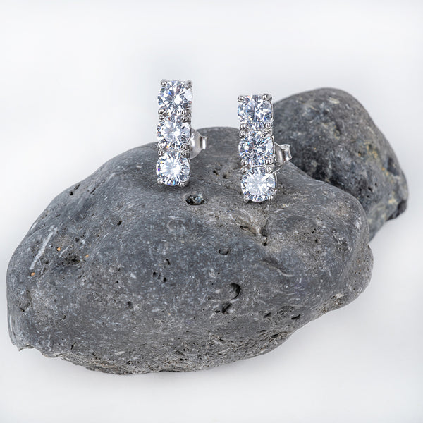 Trilogy Earrings placed on the dark grey rock, in the center of the image against a white background. 