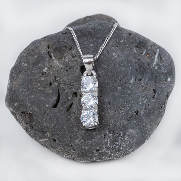 A silver Trilogy necklace with a single AAA cubic zirconia gemstone pendant set in a silver cap, displayed on a textured gray rock.