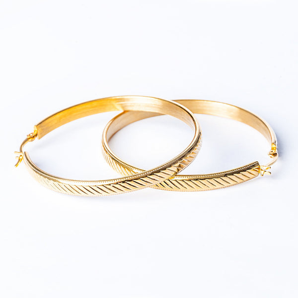 A pair of yellow gold stainless steel hoop earrings with a textured design, displayed on a white background.