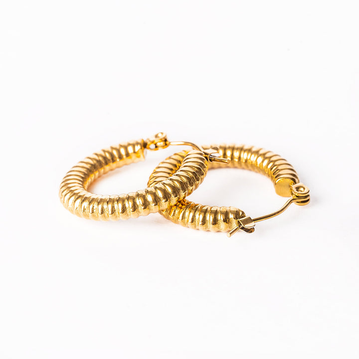 A close up view of vivi gold earrings standing in the center of the image against a white background. 