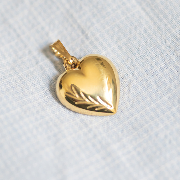 A gold-plated heart-shaped pendant on a chain against a white background