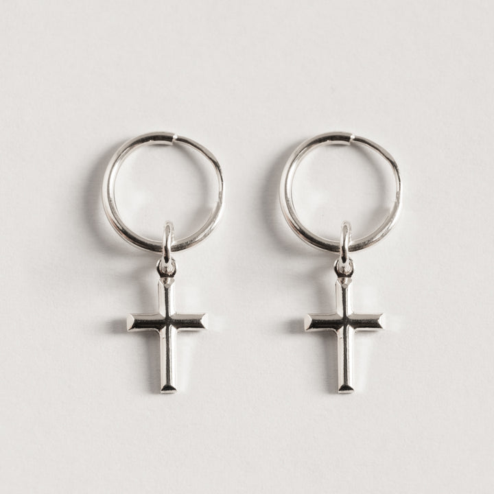 A pair of sterling Cross Silver Huggies earrings with a cross design.