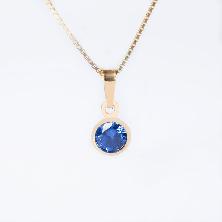 A yellow gold-plated sterling December Birth Stone pendant featuring a blue tanzanite cubic zirconia, attached to a gold-plated chain.