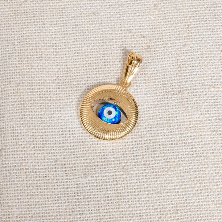 A gold-colored round eye evil pendant with a blue and white pattern resembling an eye, displayed on a textured background.