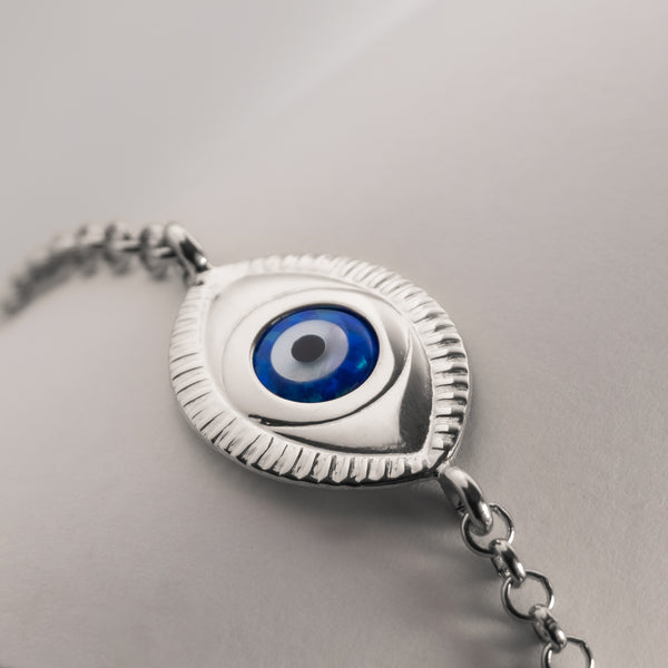 A silver bracelet featuring an evil eye design with a blue and silver color scheme on a chain structure.