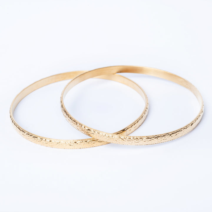 A pair of yellow gold-plated stainless steel bangle bracelets designed with a filigree pattern.