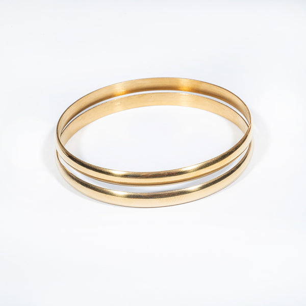 A pair of yellow gold plain bangles on a white background
