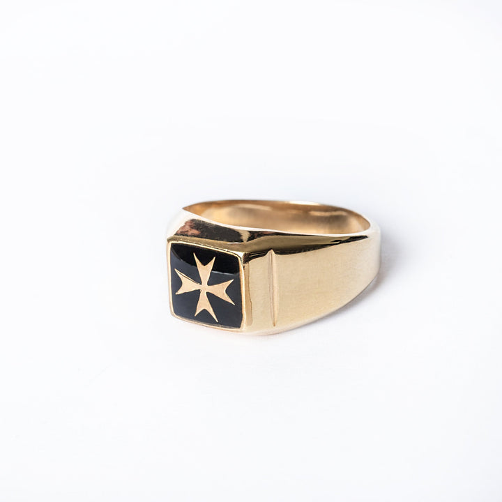 A gold-plated silver Gianni ring with a black Maltese cross emblem on it, displayed against a white background.