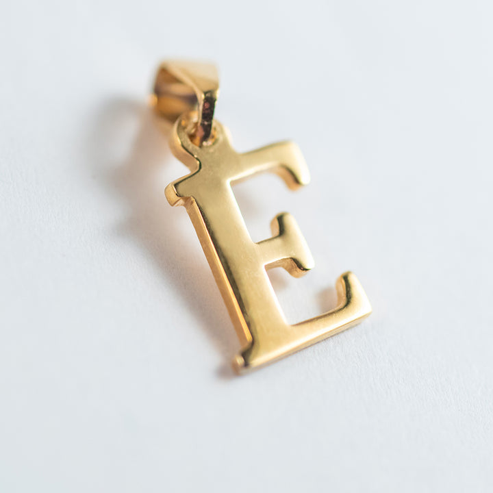 A close up view of gold letter pendant  letter  E 