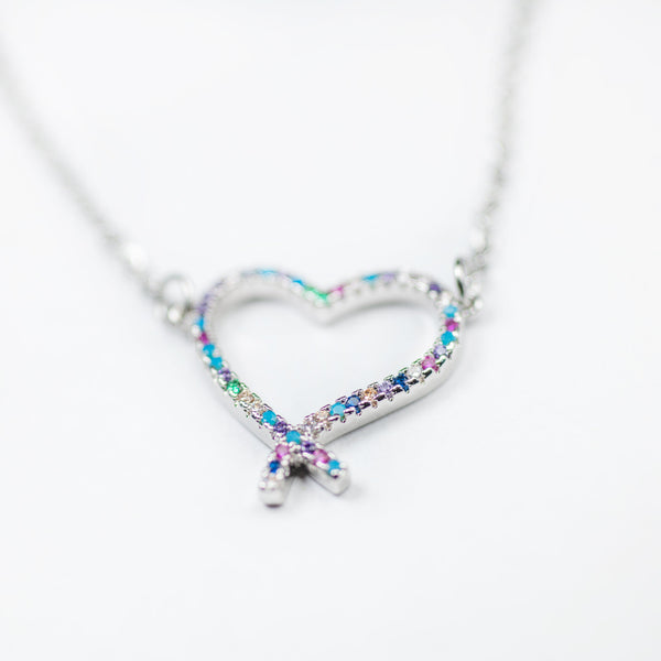 A silver-colored stainless steel necklace featuring a heart-shaped pendant adorned with multicolored cubic zirconia gems. The pendant has a reflective surface and is attached to a silver chain.