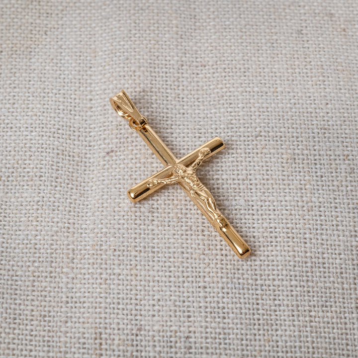 A gold-plated sterling silver cross pendant laid on a textured fabric surface.