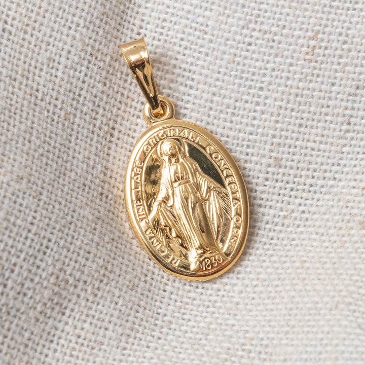 A close up view of holy mary medal double sided pendant placed on the white creamy fabric ( cloth ). 