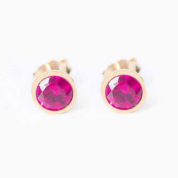 A pair of July Birthstone stud earrings with yellow gold plating, featuring a red ruby-colored gemstone.