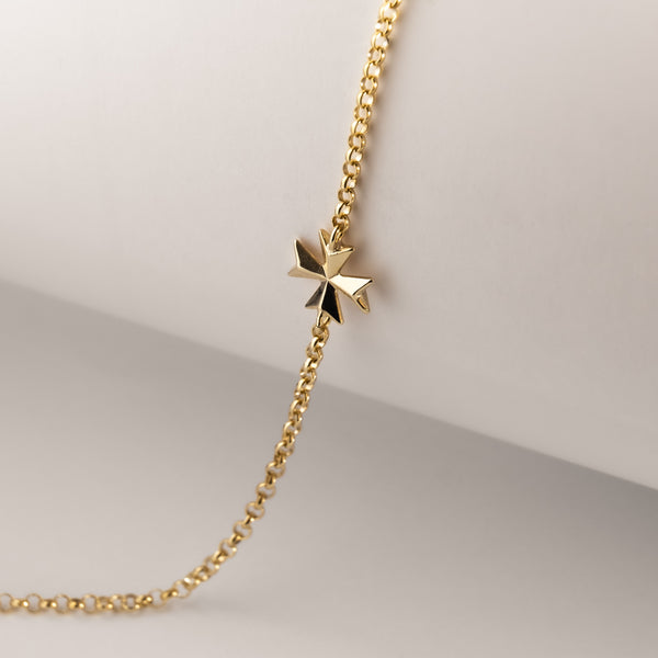A gold-plated Malta cross bracelet with a Maltese cross design on a chain structure, displayed on a mannequin.