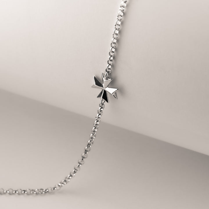 A silver Malta cross bracelet featuring a single star-shaped charm, displayed on a chain against a mannequin bust.